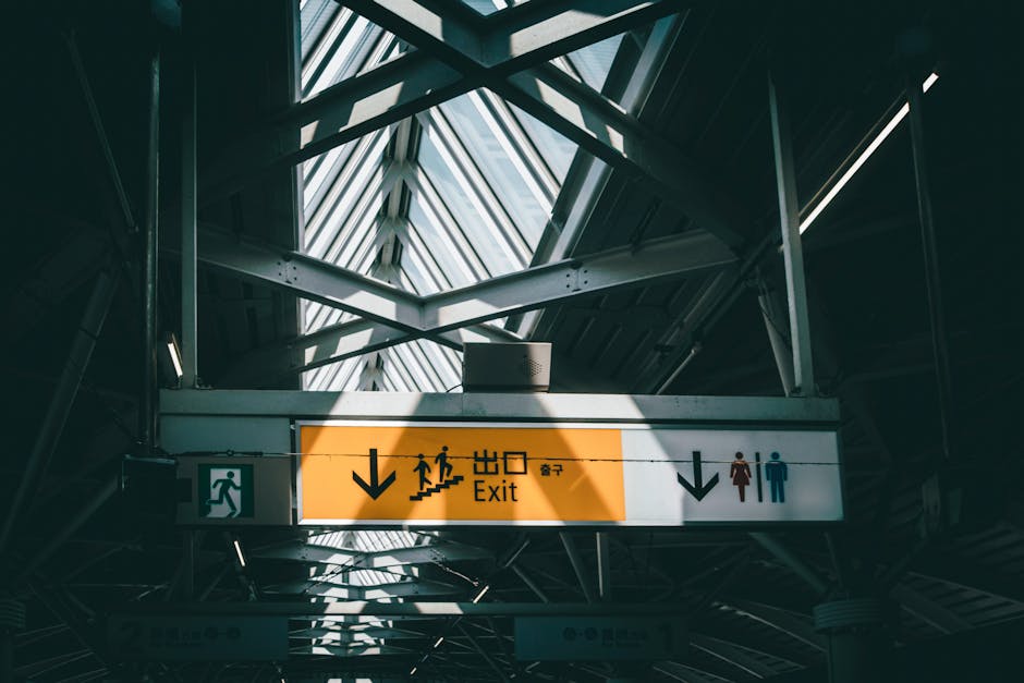 The image depicts a busy train station entrance with a wide set of grey concrete stairs leading up to a platform, framed by stainless steel handrails on each side. Several commuters are ascending the